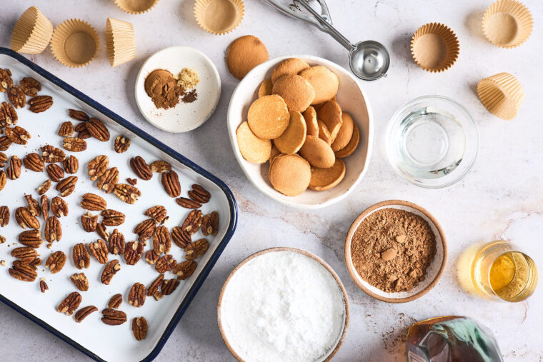 An overhead of ingredients including toasted pecans, nilla wafers, coca powder and more on a white countertop