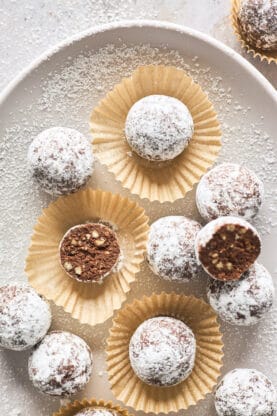 Kentucky bourbon balls coated in powdered sugar with one cut in half against a beige platter