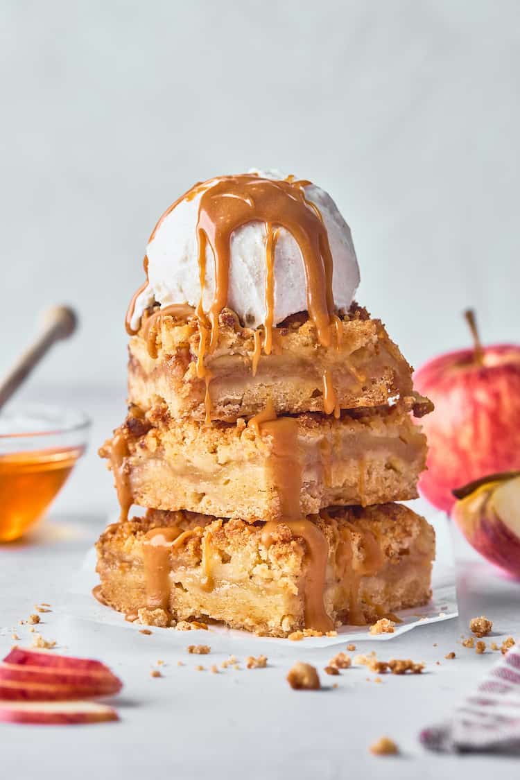 A stack of three apple bars with a scoop of vanilla ice cream and honey caramel on top