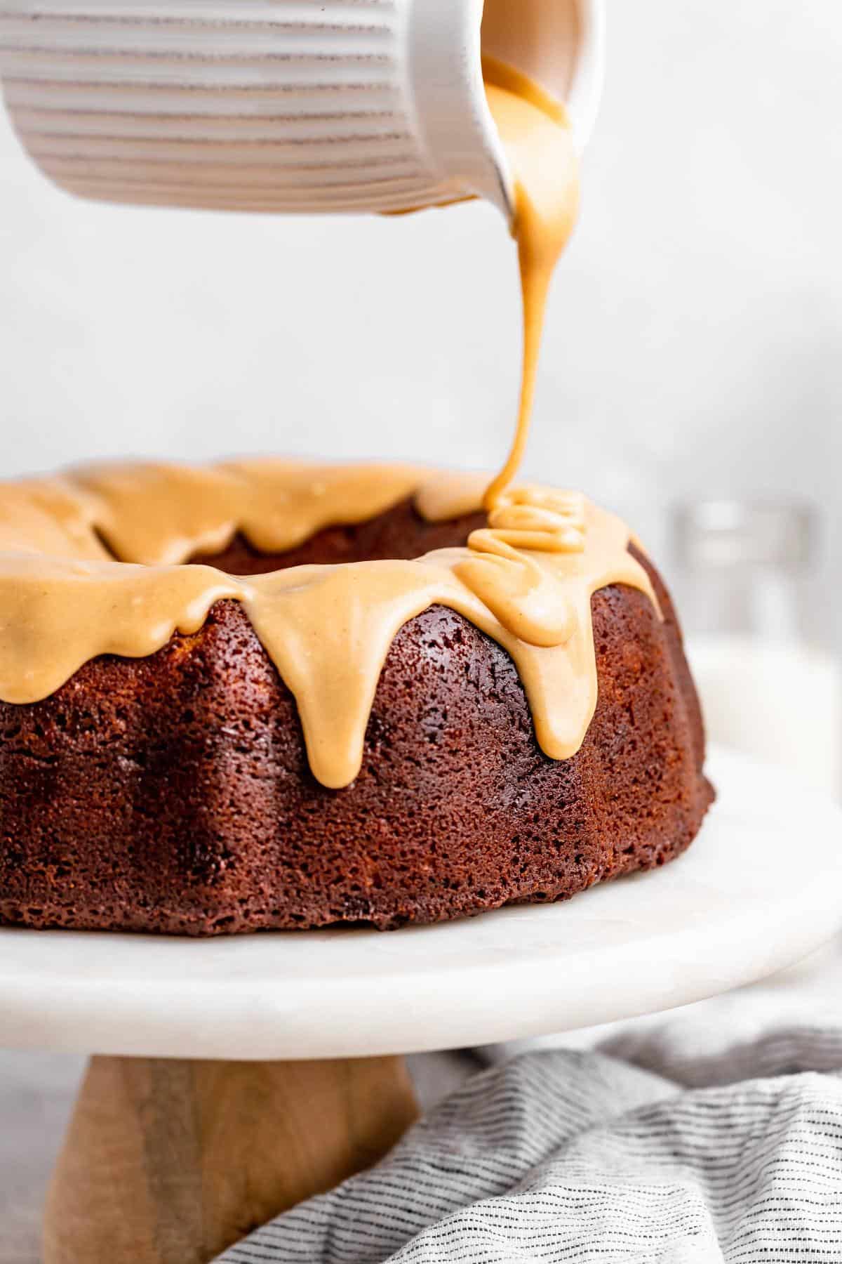 A close-up of golden caramel icing being poured over a rich milky way cake on a white cake stand