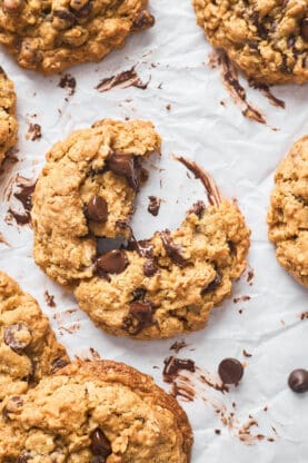 A close up of baked oatmeal chocolate chip cookies with one split apart with chocolate oozing out