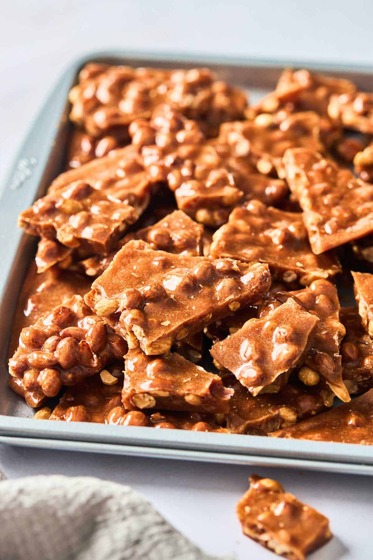A close up of the best peanut brittle on a baking sheet after being broken apart.