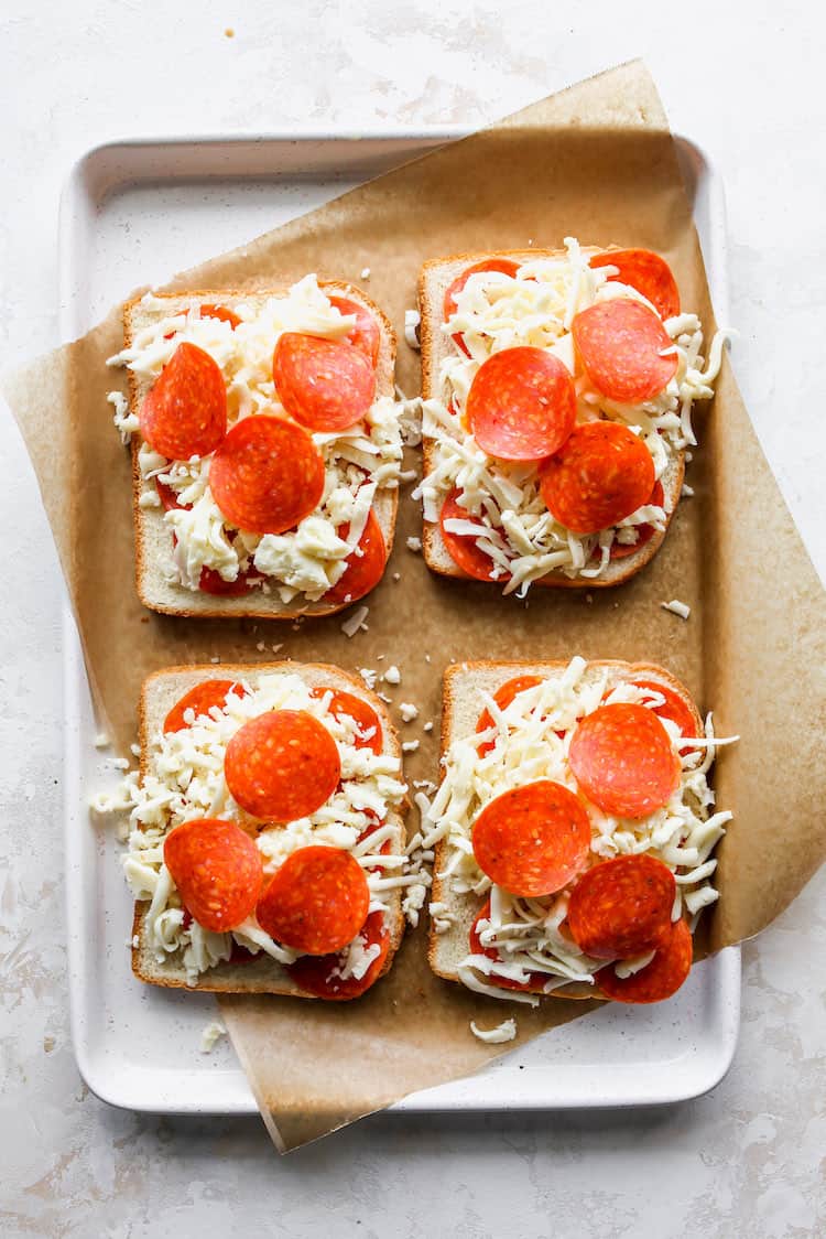 Four slices of bread with mozzarella cheese and pepperoni slices before baking