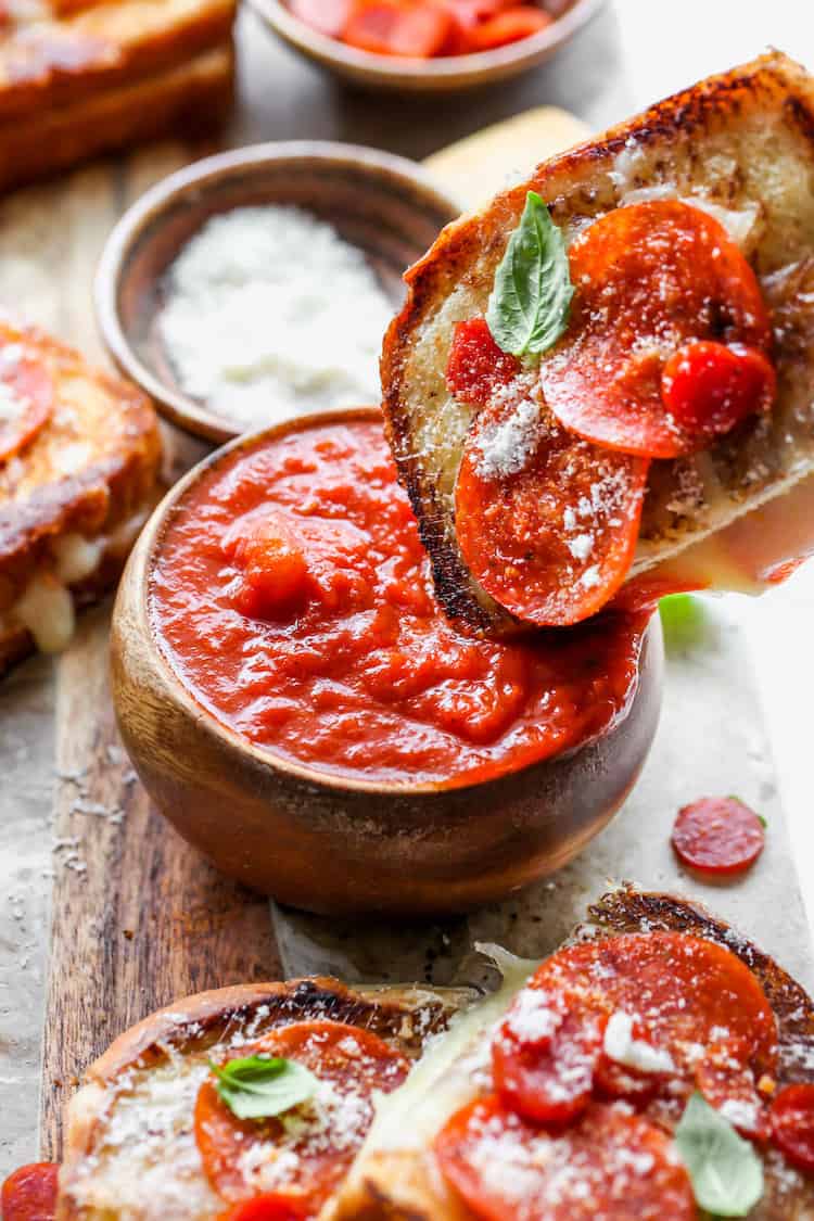 A pizza grilled cheese sandwich piece being dipped into marinara sauce before eating