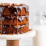 Three-layer pumpkin spice turtle cake on a marble cake stand with glossy chocolate and caramel drips and chopped pecans on top