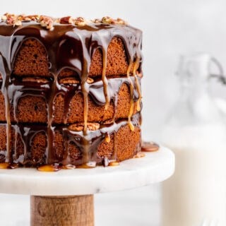 Three-layer pumpkin spice turtle cake on a marble cake stand with glossy chocolate and caramel drips and chopped pecans on top