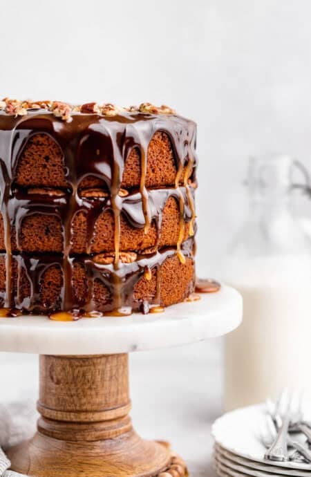 Three-layer pumpkin spice turtle cake on a marble cake stand with glossy chocolate and caramel drips and chopped pecans on top