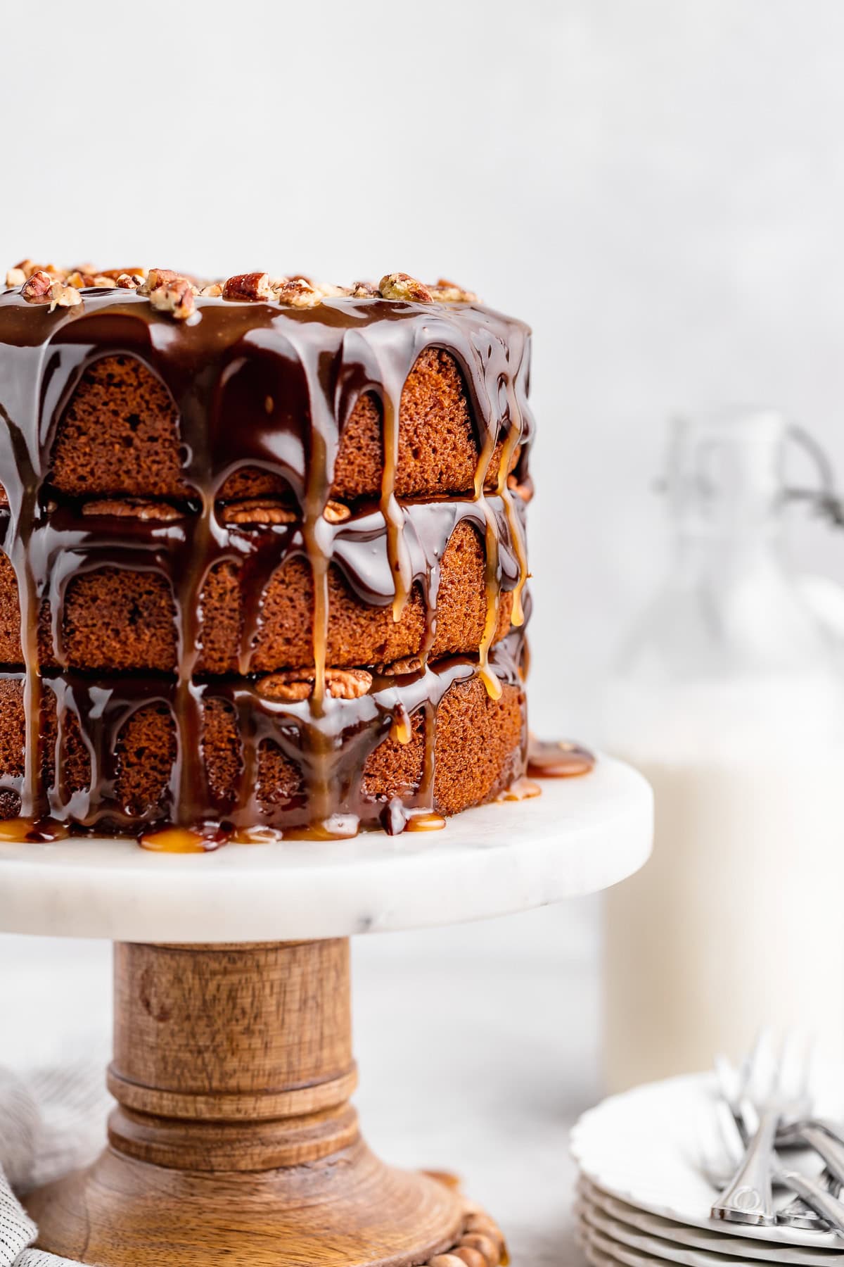 Three-layer pumpkin spice turtle cake on a marble cake stand with glossy chocolate and caramel drips and chopped pecans on top