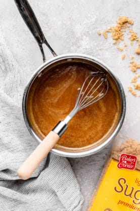 Caramel sauce being whisked in a silver pot with brown sugar nearby