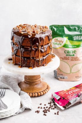 A pumpkin spice turtle cake on a white and wooden cake stand with brown sugar and chocolate chips from ALDI in the background
