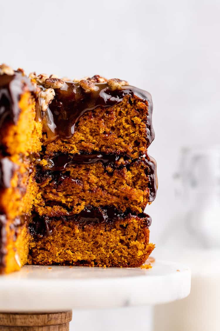 A close up of a pumpkin spice turtle cake sliced with chocolate dripping down