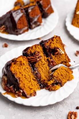 A slice of pumpkin cake with chocolate and caramel sauces and pecans with a fork slicing through