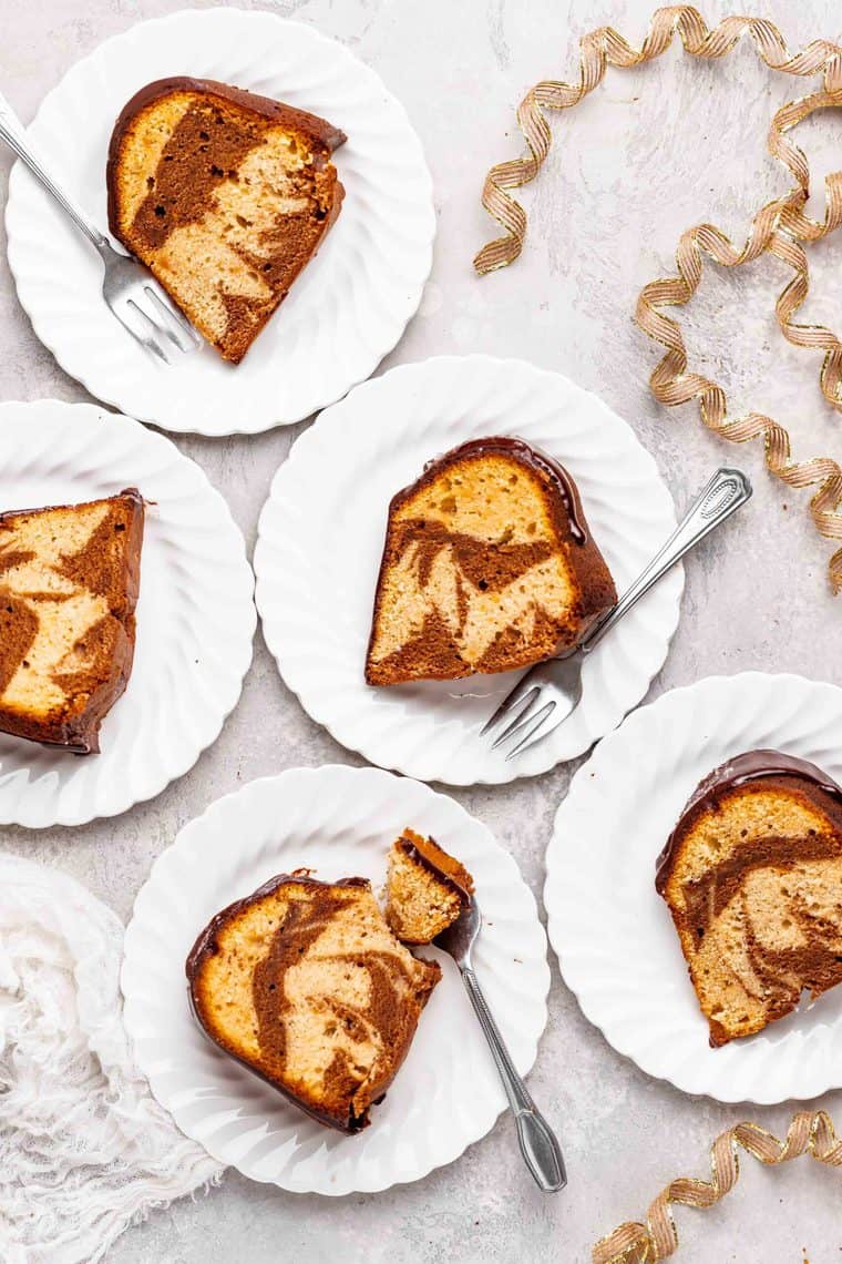 An overhead of white plates with marble cake slices and forks ready to serve