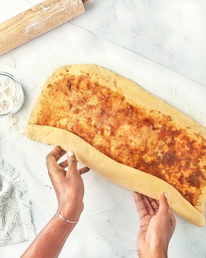 Two hands rolling dough after adding cinnamon sugar filling