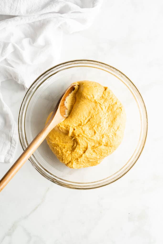 Sweet potato dough in a clear bowl with a spoon after bring together to rise