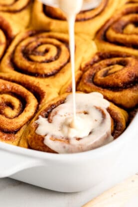 Brown butter cream cheese glaze drizzling over the top of baked cinnamon rolls
