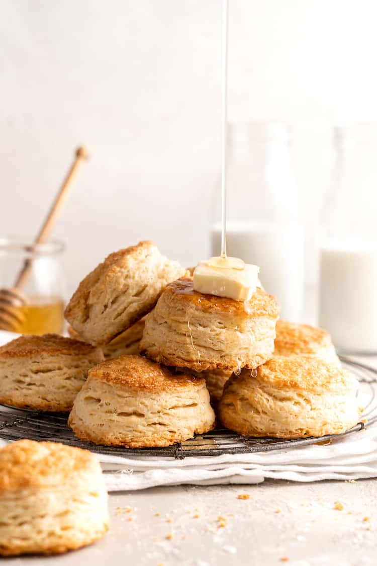 Stacks of super flaky biscuits with butter on top and honey being drizzled on top against white background