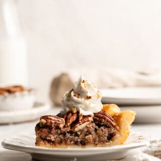 A slice of chocolate pecan pie sitting on a white plate with whipped cream on top against white background