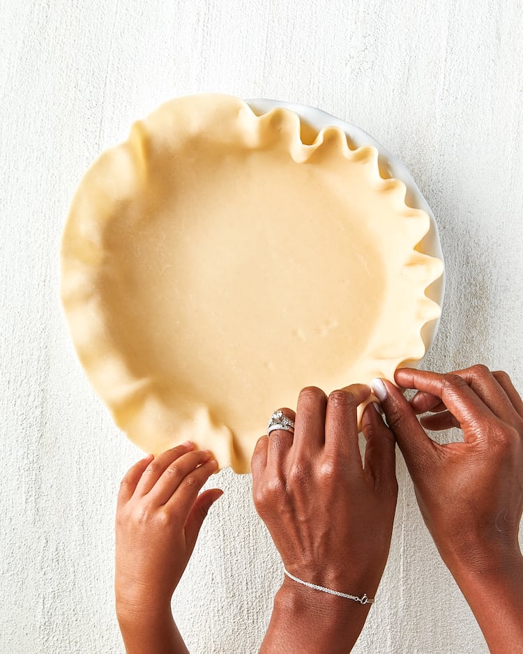 Jocelyn Delk Adams and her daughter crimping a pie crust against white background