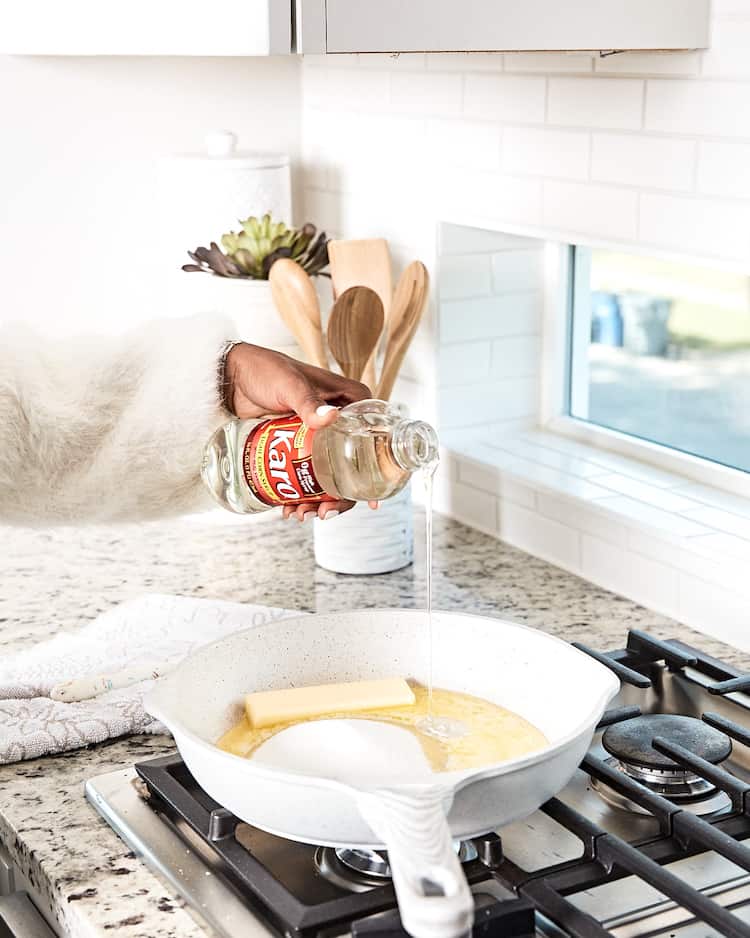 A hand pouring corn syrup into a white cast iron skillet to make pie filling