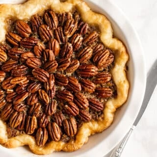 A full shot of a chocolate bourbon pecan pie recipe on a white countertop with a knife nearby