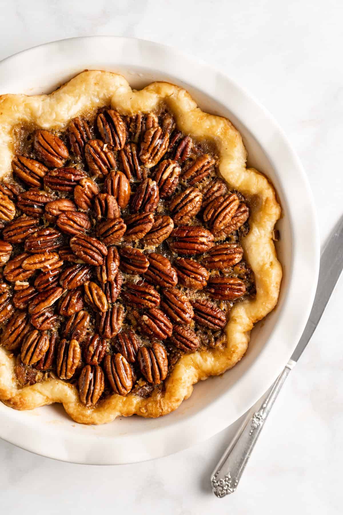 A full shot of a chocolate bourbon pecan pie recipe on a white countertop with a knife nearby