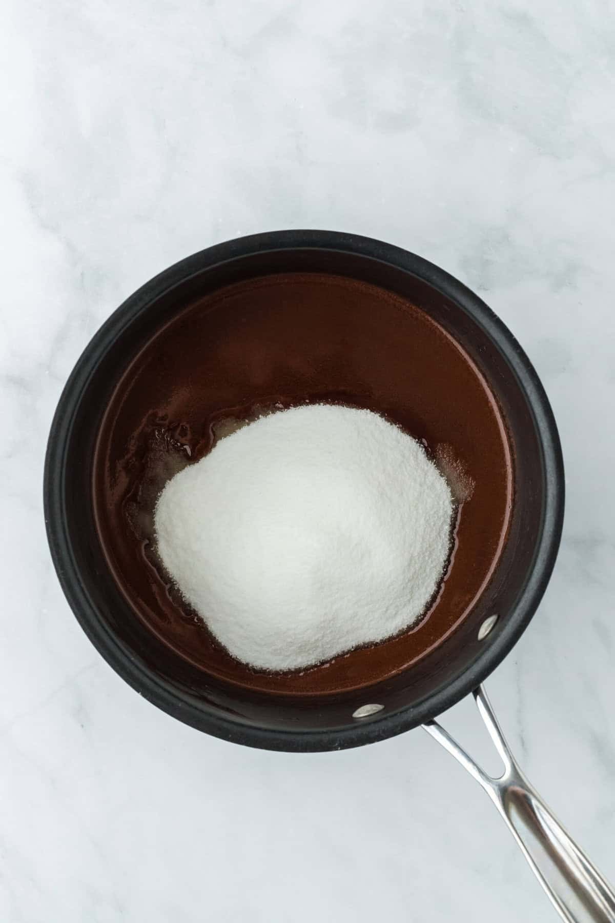 Sugar added to melted chocolate in small pot on white background