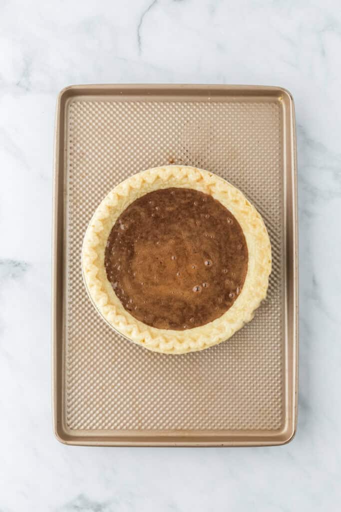 Chocolate pie filling added to pie crust on a baking sheet on white countertop