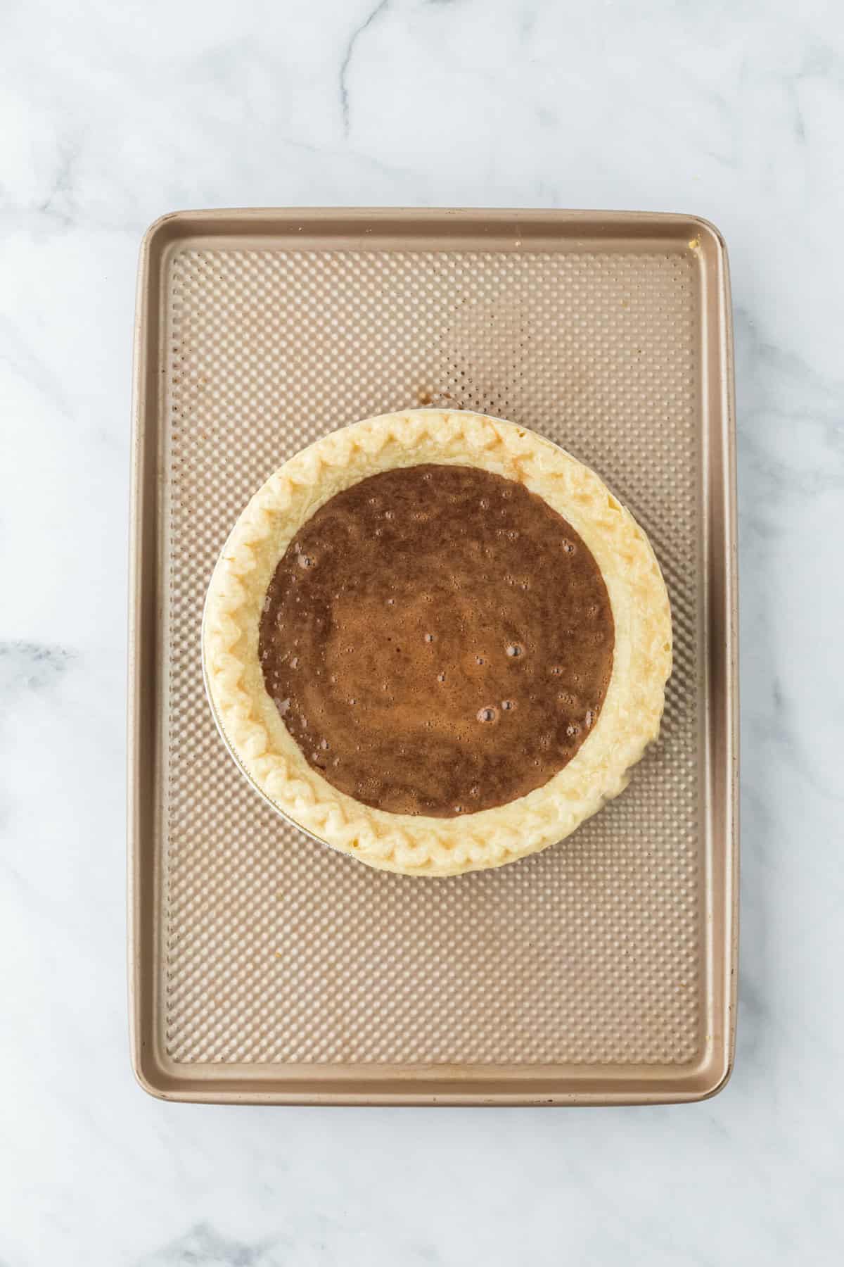 Chocolate pie filling added to pie crust on a baking sheet on white countertop