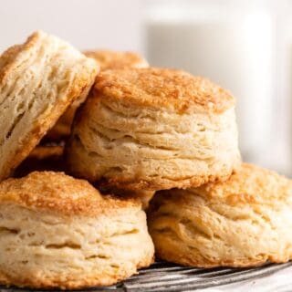 Closeup of golden, flaky biscuits stacked on a wire rack with a soft background