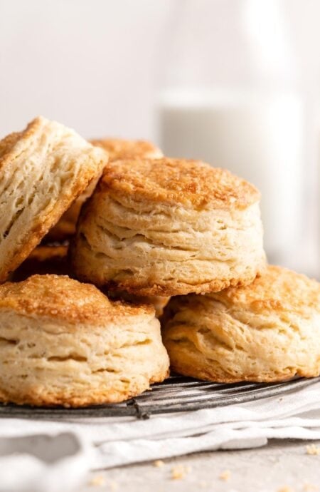Closeup of golden, flaky biscuits stacked on a wire rack with a soft background