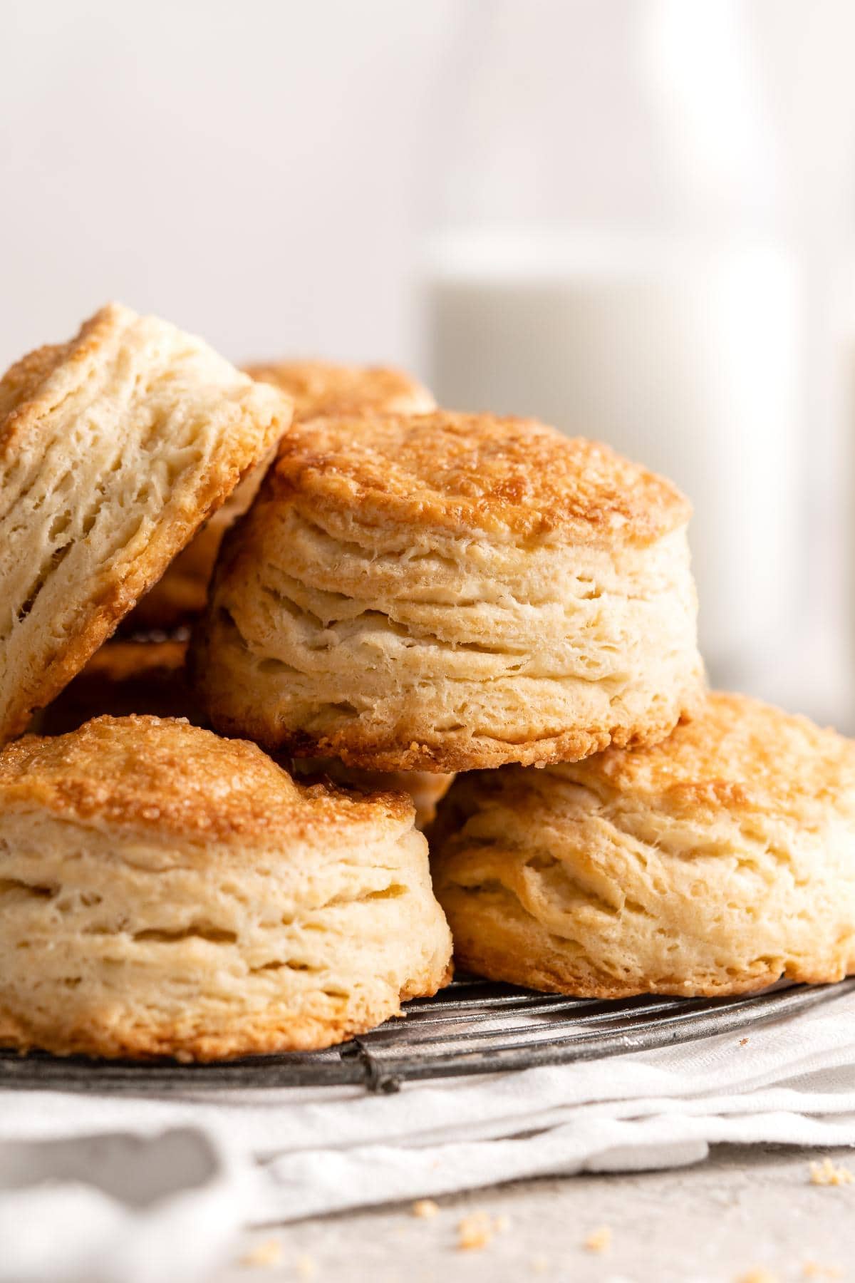 Closeup of golden, flaky biscuits stacked on a wire rack with a soft background