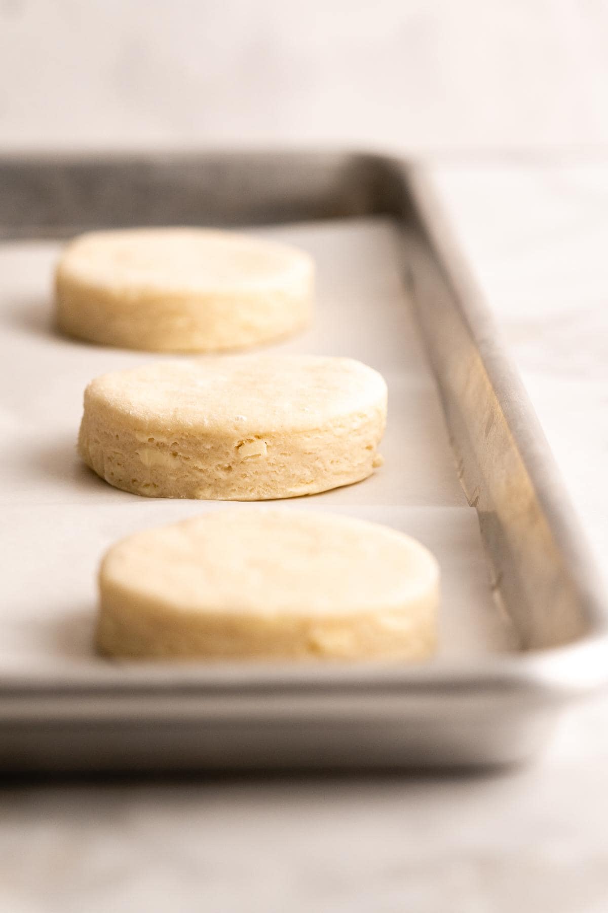 Unbaked biscuit rounds placed on a baking sheet lined with parchment paper