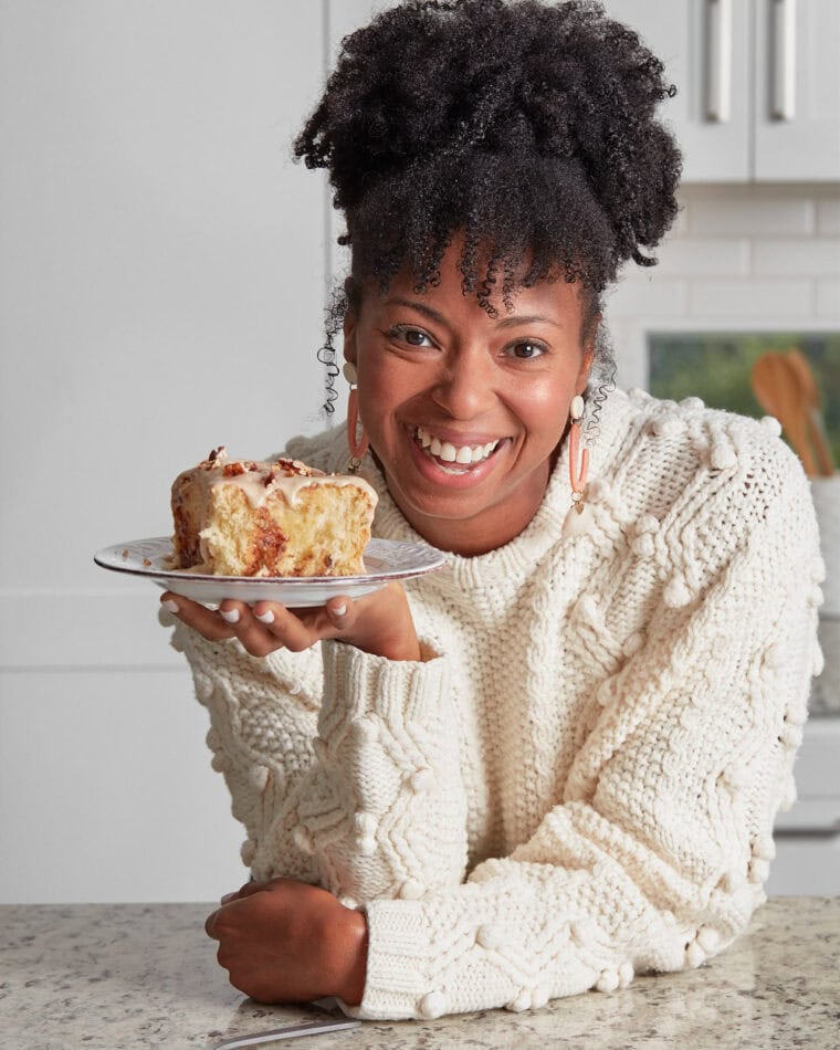 Jocelyn Delk Adams holding a sweet potato cinnamon roll on a plate smiling