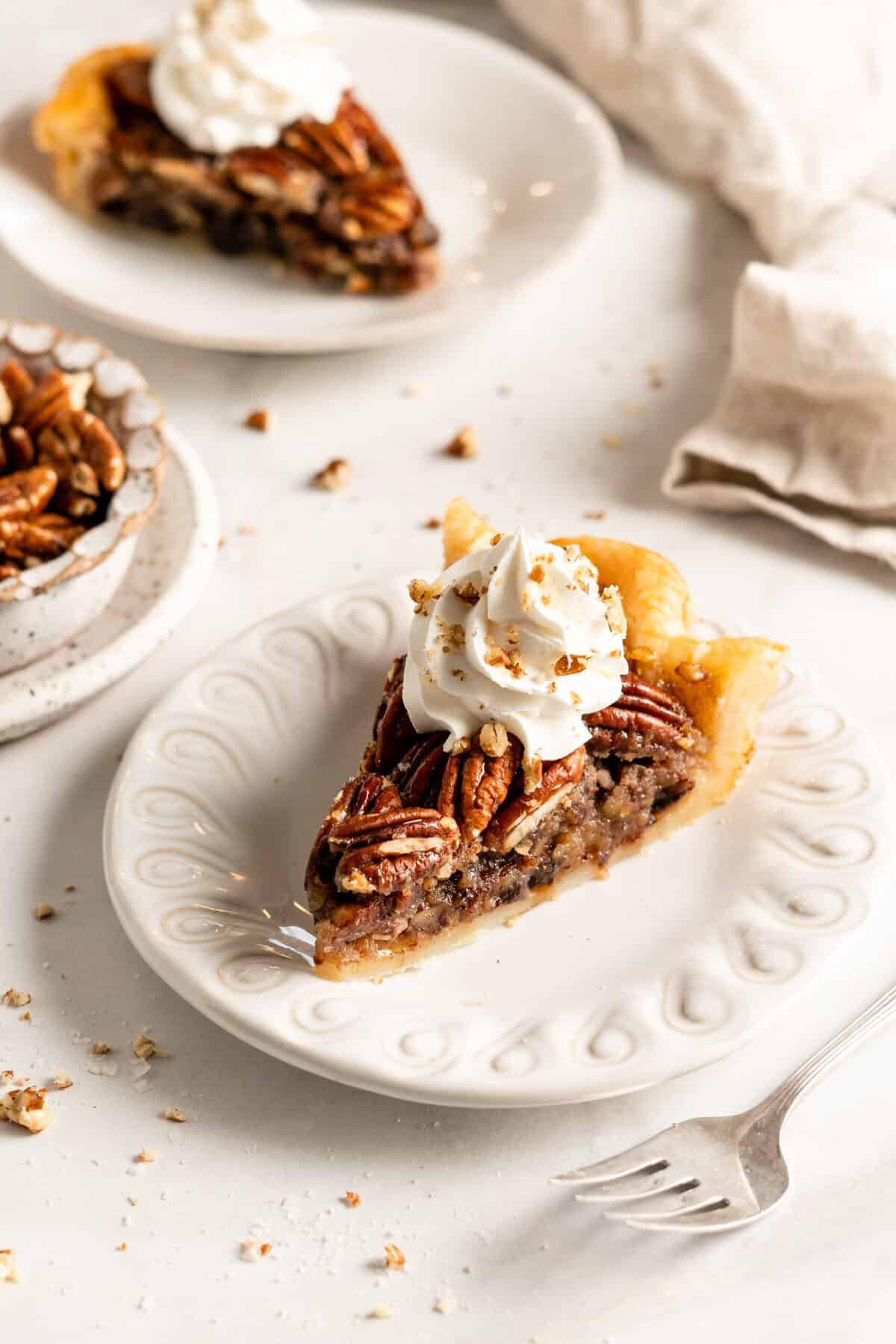 Slices of bourbon chocolate pecan pie with whipped cream on white plates on white background