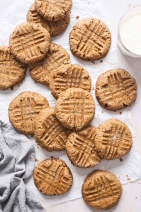 Fresh peanut butter cookies scattered against white background with a gray towel