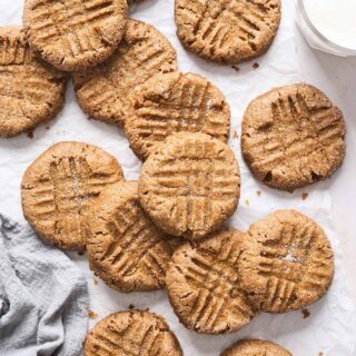 Fresh peanut butter cookies scattered against white background with a gray towel