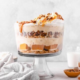 A trifle filled with sweet potato pie and pecan pie with ice cream and caramel sauce on top against a white background