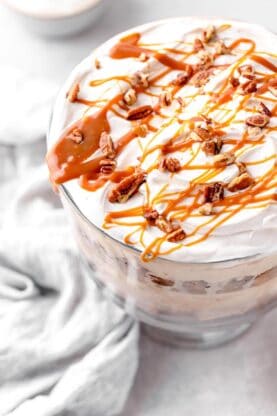 A close up of a pie trifle with caramel sauce and pecans drizzled on top against a white background