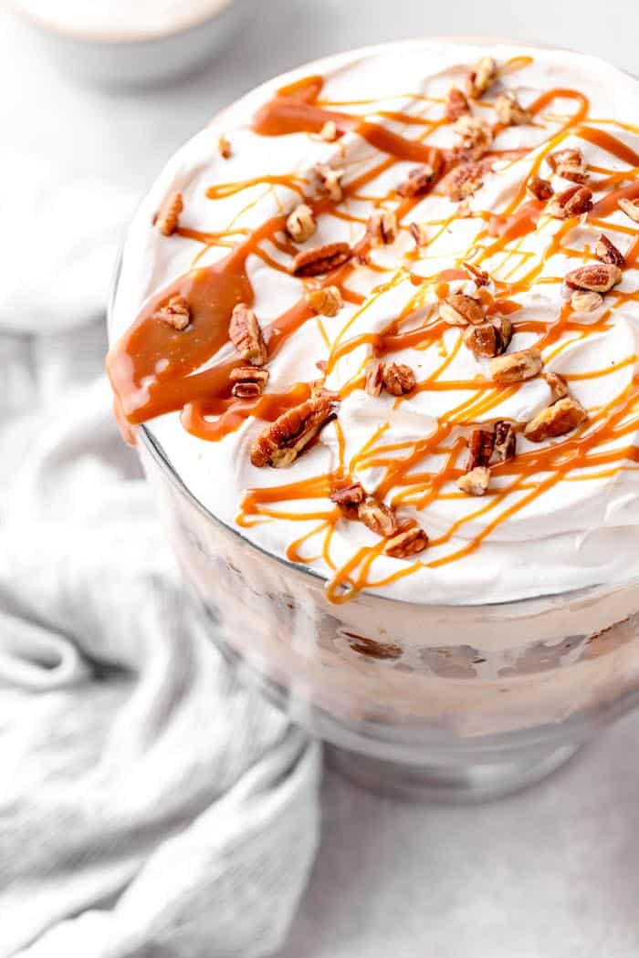 A close up of a pie trifle with caramel sauce and pecans drizzled on top against a white background