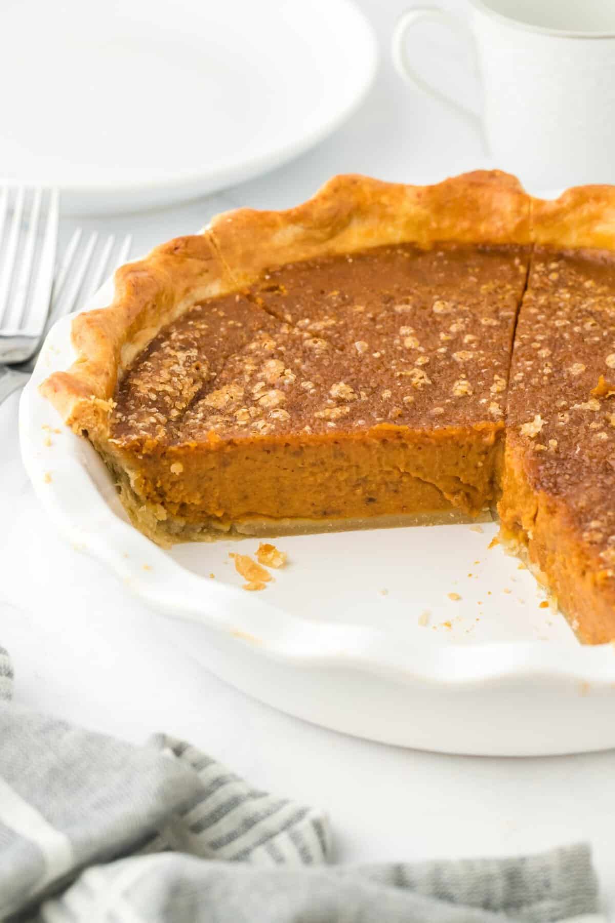 A full pumpkin pie with a slice cut out, showcasing the flaky crust and creamy filling