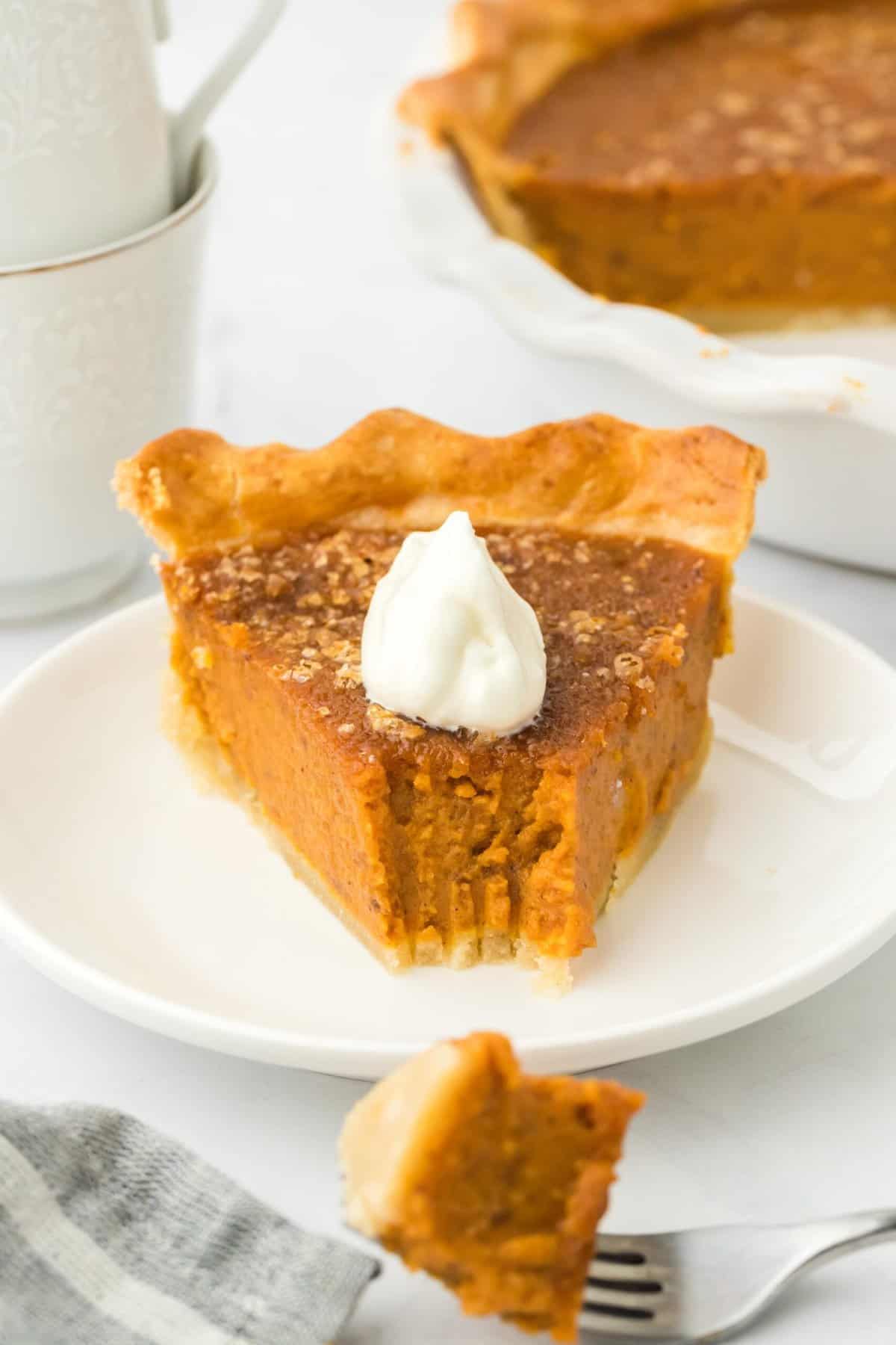  A slice of pumpkin pie with a bite taken out on a plate topped with whipped cream