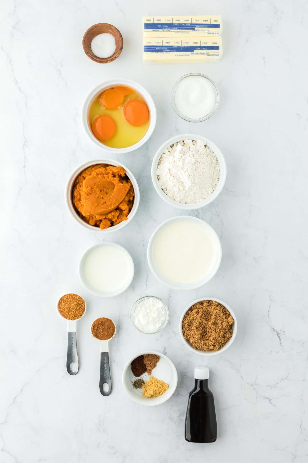 Overhead shot of ingredients to make pumpkin pie on a white surface before mixing