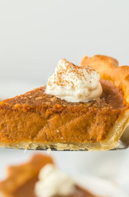 A pie server holding a slice of pumpkin pie with whipped cream on top