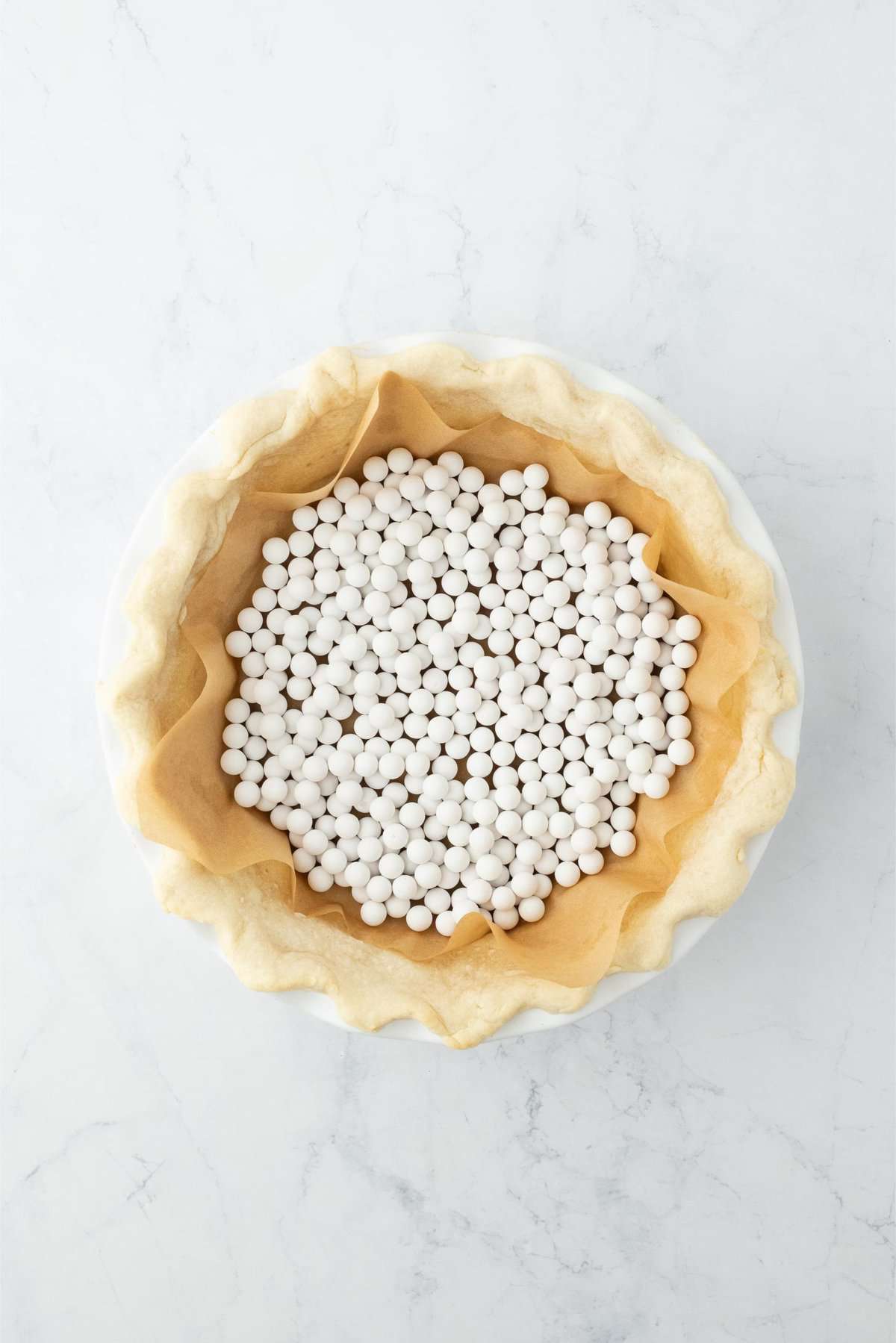 Overhead shot of a partially baked pie crust with pie weights inside