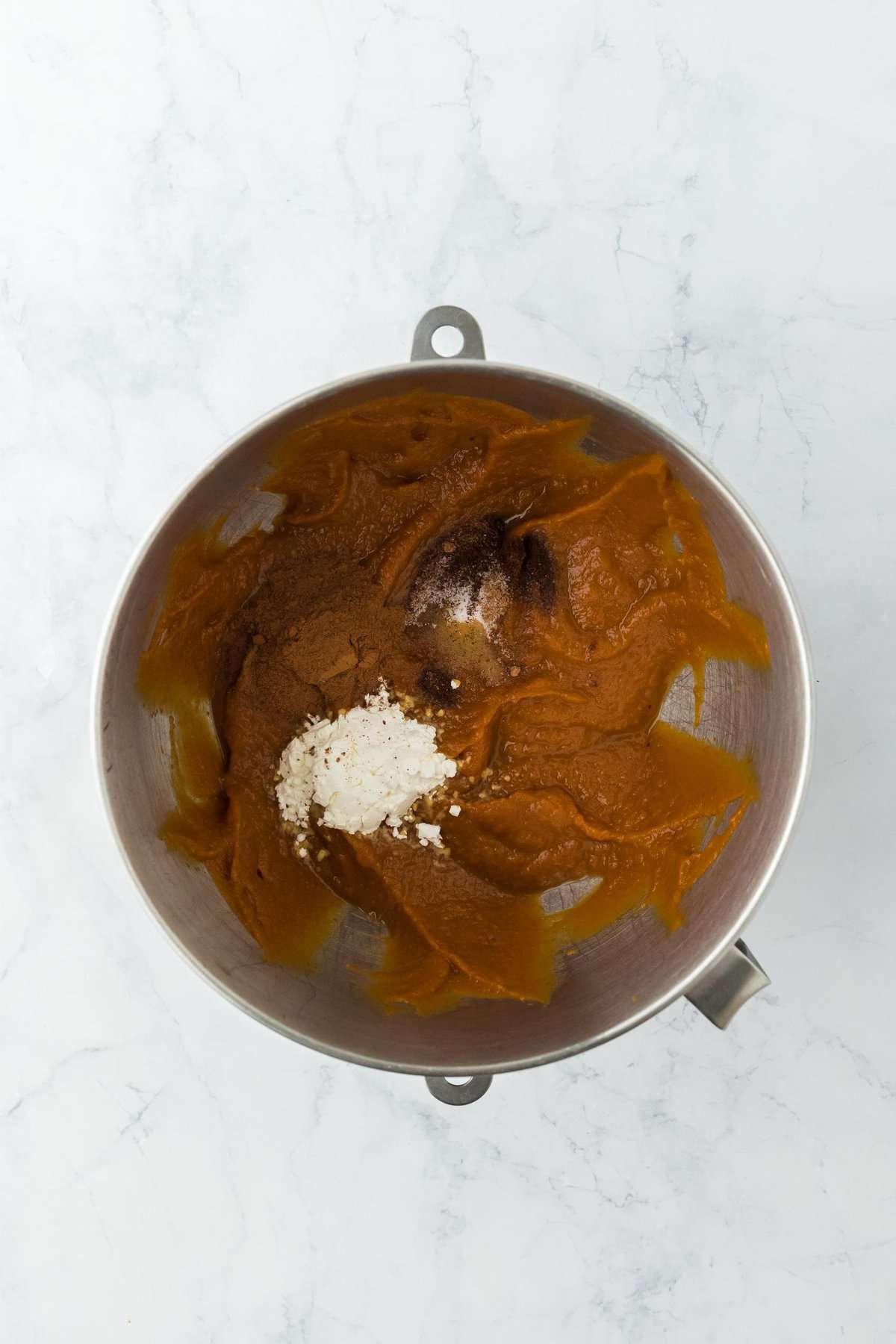 Overhead shot of a mixing bowl with pumpkin puree, spices, and other ingredients for making pumpkin pie filling