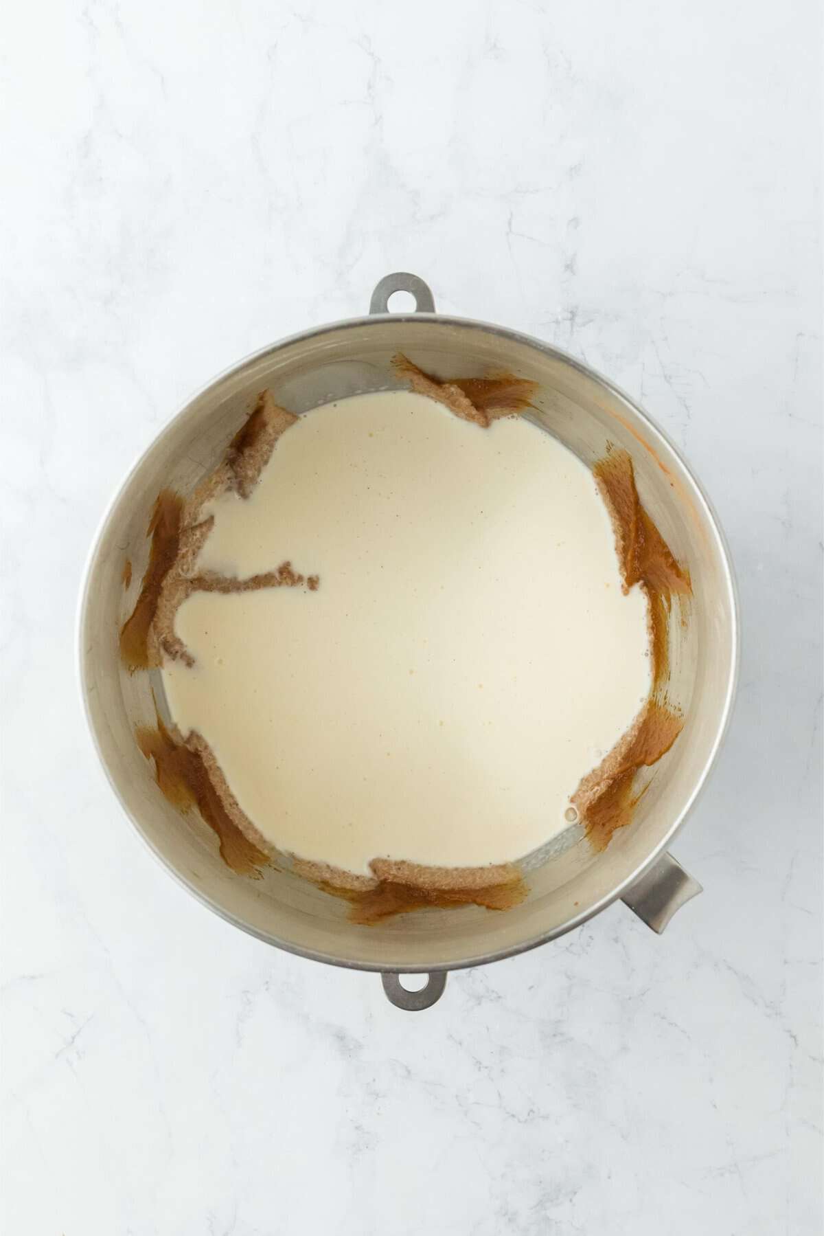 Overhead shot of a mixing bowl with a layer of heavy cream and milk, partially covering the rest of the mix