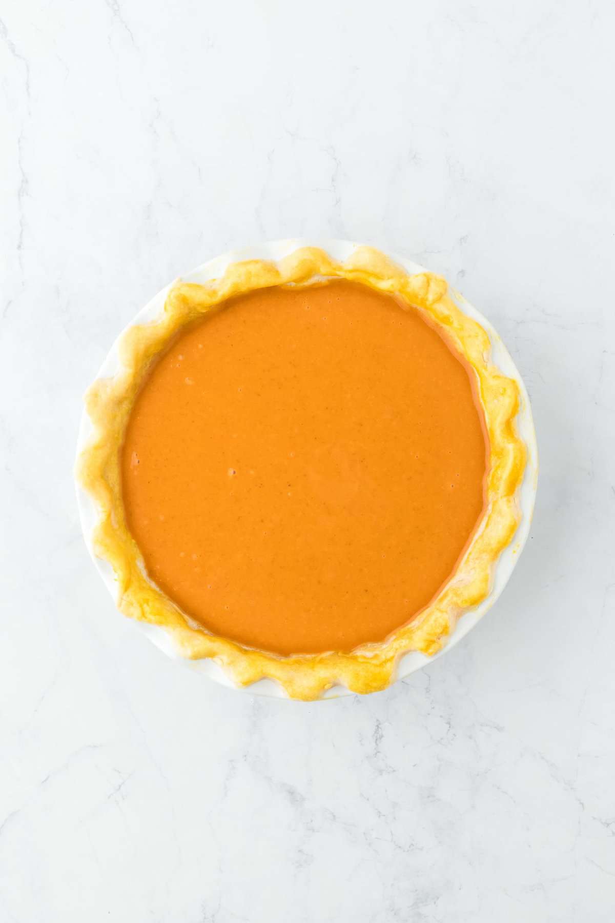 An unbaked pumpkin pie, with the filling poured evenly into the pie crust