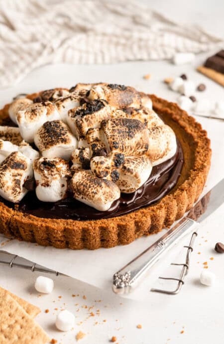 A pumpkin pie with a chocolate ganache and toasted marshmallow topping in a close up against a white background