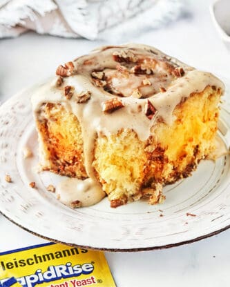 A large cinnamon roll with brown butter glaze and pecans on top of a white plate